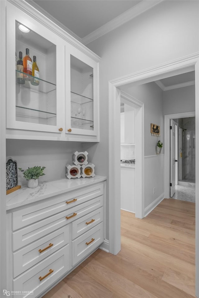 bar with white cabinetry, ornamental molding, light stone counters, and light wood-type flooring