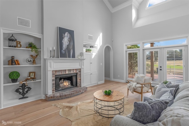 living room featuring a brick fireplace, light hardwood / wood-style flooring, ornamental molding, built in features, and a high ceiling