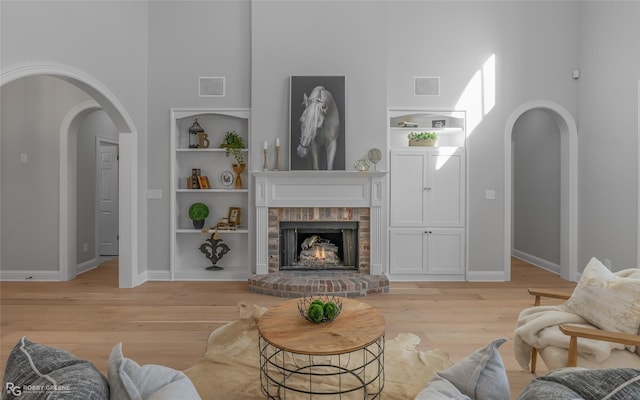 living room with a brick fireplace, built in features, light hardwood / wood-style floors, and a high ceiling