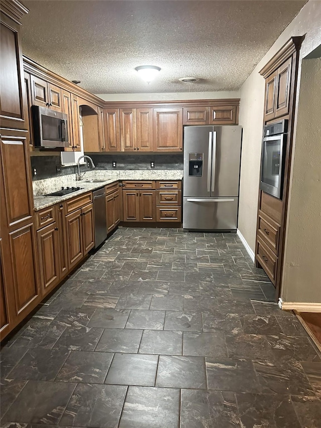 kitchen featuring a textured ceiling, stainless steel appliances, light stone counters, and sink