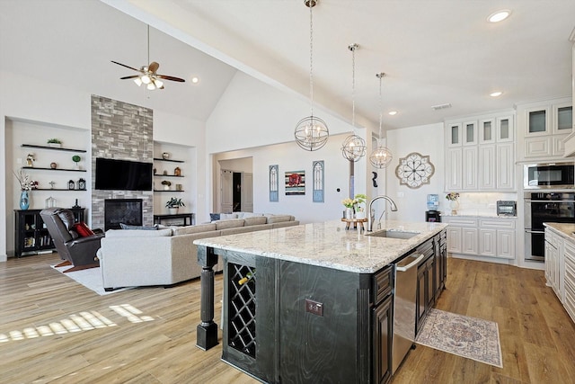 kitchen featuring white cabinetry, sink, a stone fireplace, built in features, and a kitchen island with sink