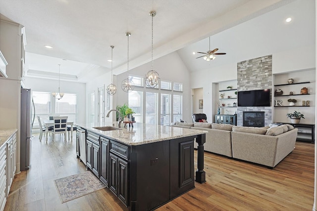 kitchen with a kitchen island with sink, sink, a large fireplace, light stone counters, and stainless steel appliances