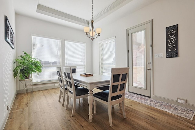 dining area featuring a raised ceiling, a wealth of natural light, a chandelier, and light wood-type flooring