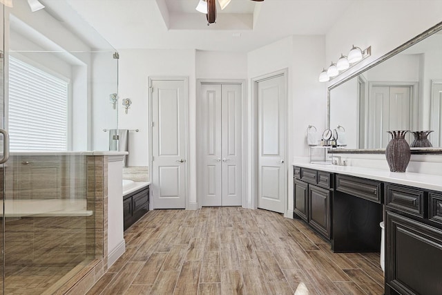 bathroom with a tray ceiling, vanity, ceiling fan, and plus walk in shower