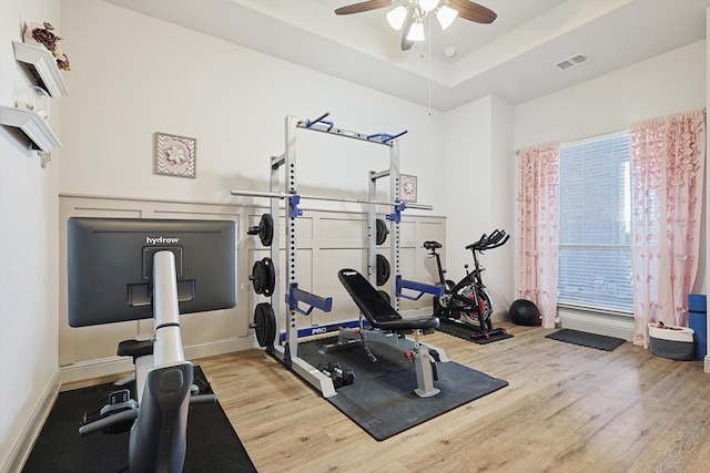 exercise area featuring light wood-type flooring, a tray ceiling, and ceiling fan