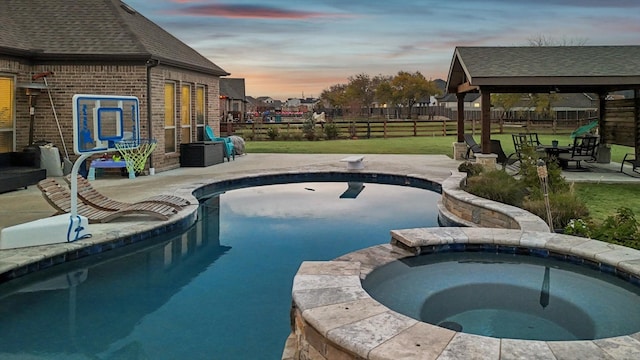 pool at dusk with an in ground hot tub, a yard, and a patio