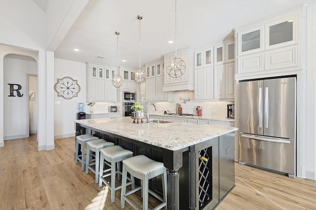 kitchen featuring a center island with sink, sink, light stone countertops, white cabinetry, and stainless steel appliances