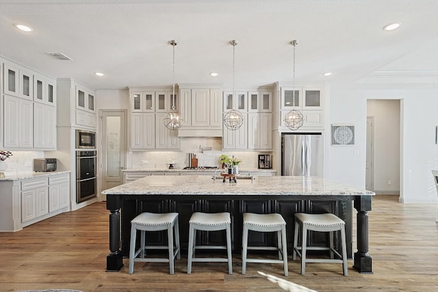 kitchen featuring appliances with stainless steel finishes, light stone countertops, an island with sink, and white cabinets