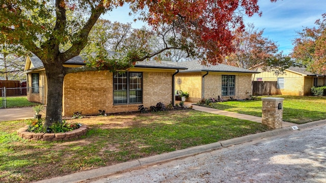 ranch-style home featuring brick siding, a front lawn, and fence
