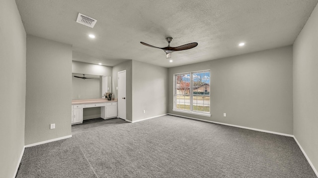 unfurnished bedroom with carpet flooring, ensuite bathroom, a textured ceiling, ceiling fan, and built in desk