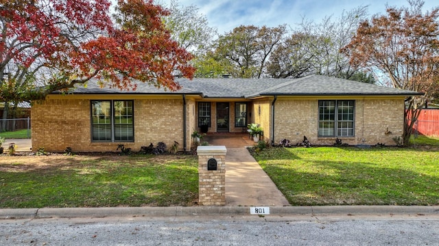 single story home featuring a shingled roof, brick siding, fence, and a front yard