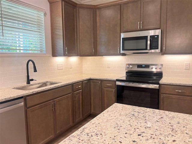 kitchen with decorative backsplash, appliances with stainless steel finishes, light stone counters, and sink