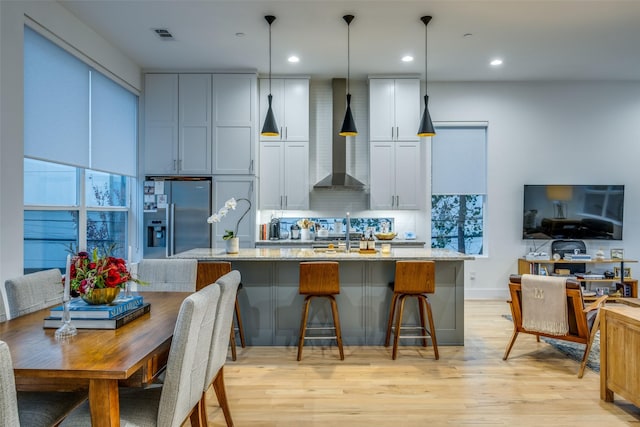 kitchen featuring tasteful backsplash, light stone counters, light hardwood / wood-style floors, decorative light fixtures, and a kitchen island with sink