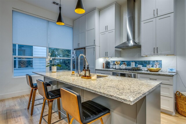 kitchen with hanging light fixtures, a kitchen island with sink, wall chimney exhaust hood, and a breakfast bar area