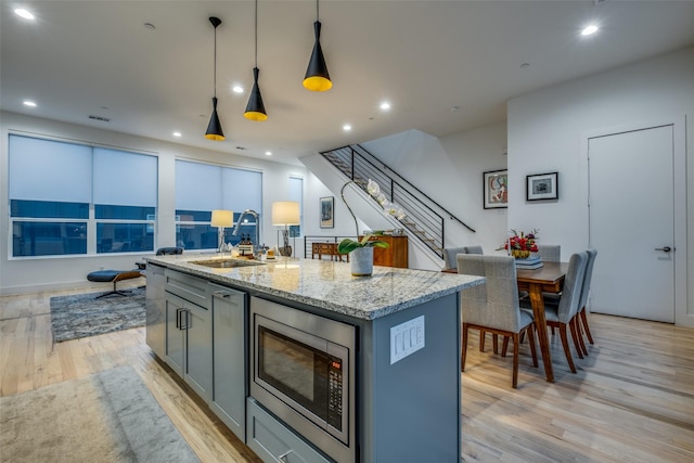 kitchen featuring light hardwood / wood-style floors, sink, a center island with sink, gray cabinets, and stainless steel microwave