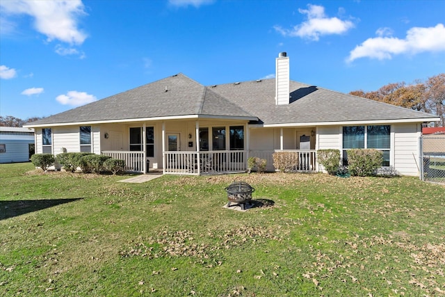 back of house featuring a porch, a fire pit, and a lawn