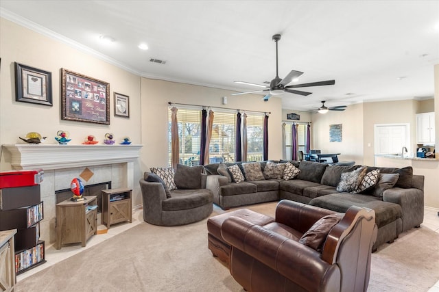 carpeted living room with a tile fireplace, crown molding, sink, and ceiling fan