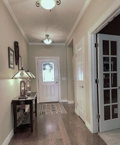 doorway to outside with ornamental molding, baseboards, and wood finished floors