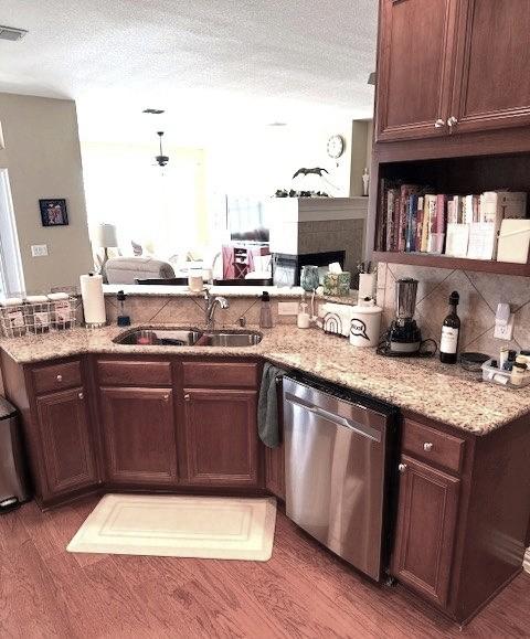 kitchen with stainless steel dishwasher, dark hardwood / wood-style flooring, sink, light stone counters, and a textured ceiling