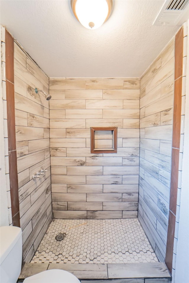 bathroom featuring toilet, a textured ceiling, and a tile shower