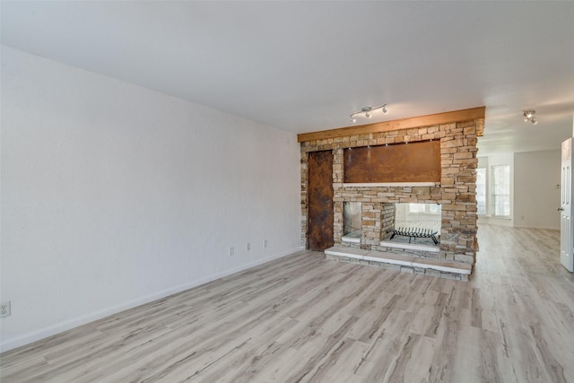 unfurnished living room featuring a stone fireplace and light hardwood / wood-style floors