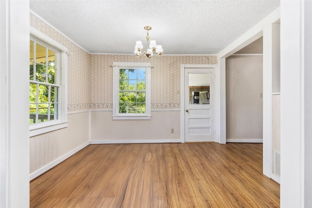 empty room with a notable chandelier, crown molding, a textured ceiling, and light wood-type flooring