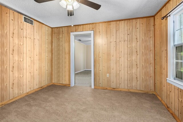 carpeted empty room featuring ceiling fan, wooden walls, and a textured ceiling