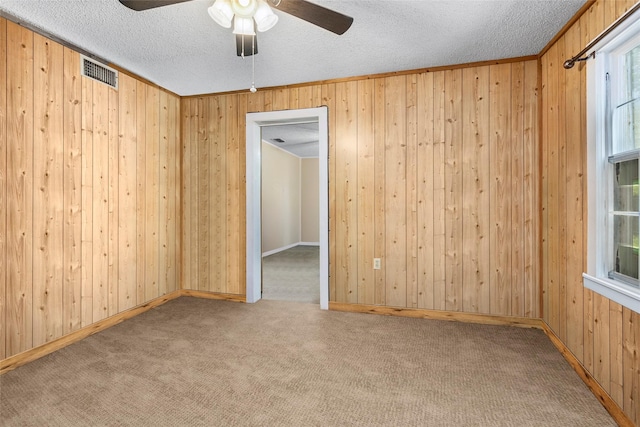 carpeted empty room featuring ceiling fan, wooden walls, and a textured ceiling