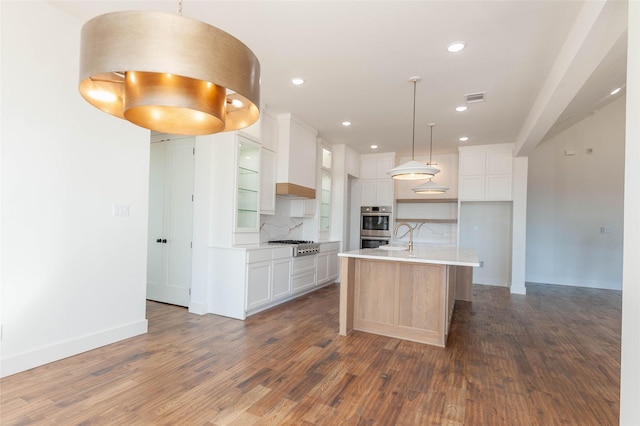 kitchen featuring white cabinetry, decorative light fixtures, a center island with sink, stainless steel appliances, and decorative backsplash