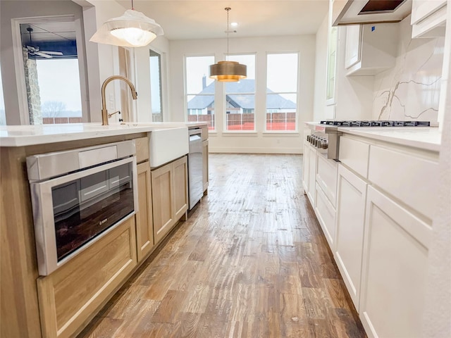 kitchen with wall chimney range hood, stainless steel appliances, decorative light fixtures, and light wood-type flooring