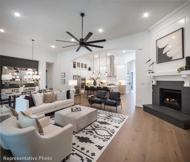 4121 Buffalo Clover Dr, Aubrey, TX 76227 - living area with arched walkways, a brick fireplace, a chandelier, a ceiling fan, and light wood-style flooring