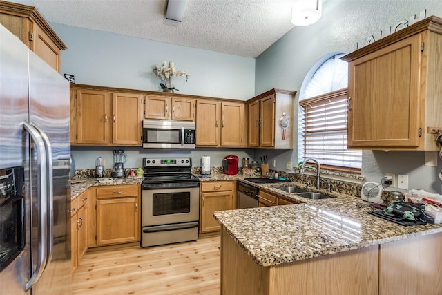 kitchen featuring sink, light wood-type flooring, a textured ceiling, appliances with stainless steel finishes, and kitchen peninsula