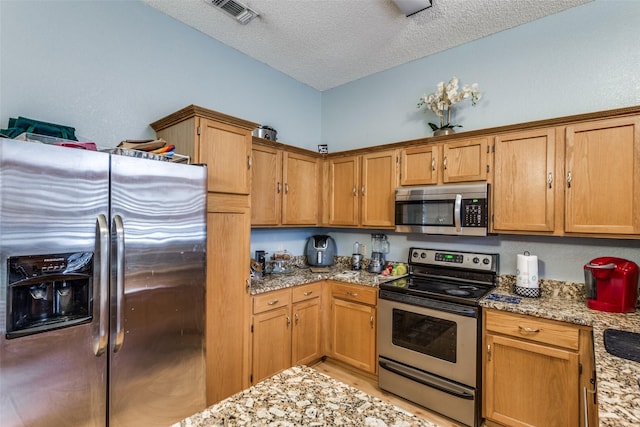 kitchen featuring light stone counters, light hardwood / wood-style flooring, a textured ceiling, and appliances with stainless steel finishes