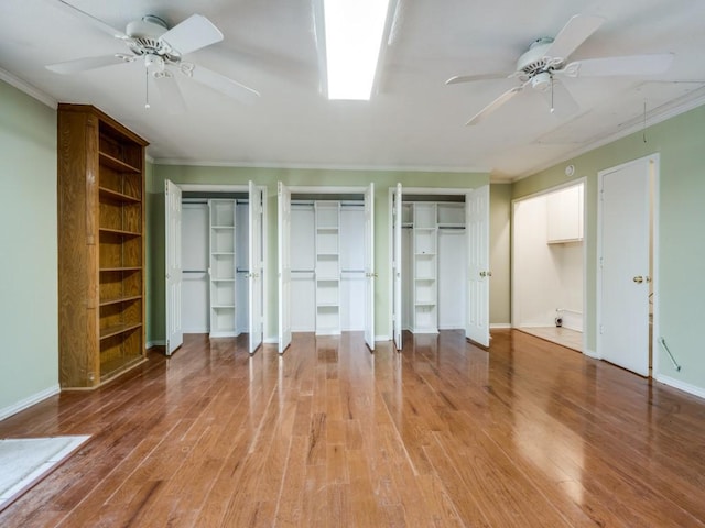 unfurnished bedroom featuring hardwood / wood-style floors, two closets, ornamental molding, and ceiling fan