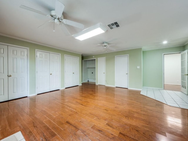 unfurnished bedroom featuring ceiling fan, ornamental molding, light hardwood / wood-style floors, and two closets