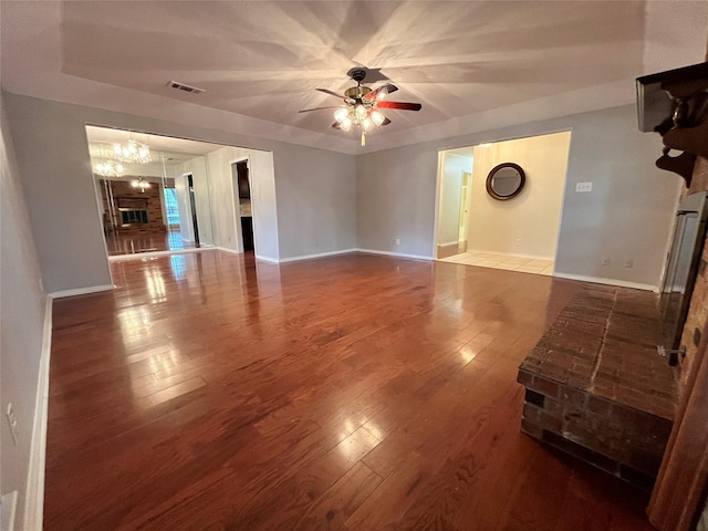 unfurnished living room featuring hardwood / wood-style flooring, ceiling fan with notable chandelier, and a brick fireplace