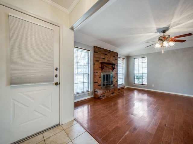 unfurnished living room featuring ceiling fan, ornamental molding, a brick fireplace, and light hardwood / wood-style flooring