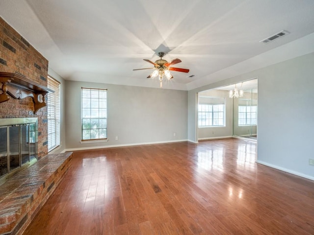 unfurnished living room with wood-type flooring, a brick fireplace, and ceiling fan with notable chandelier