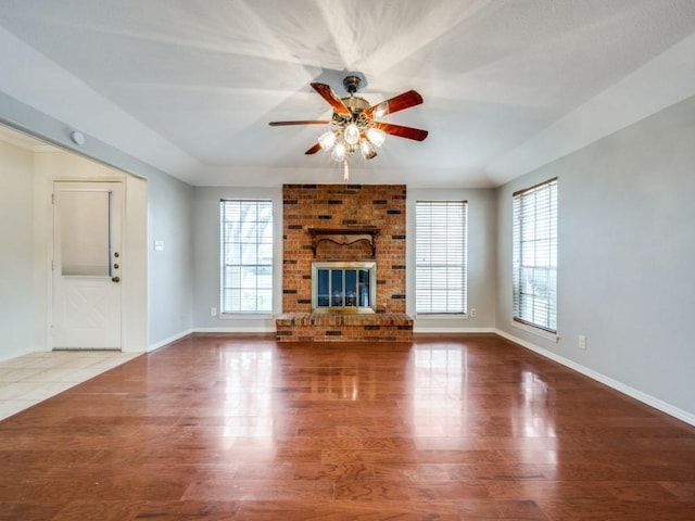 unfurnished living room featuring a healthy amount of sunlight, ceiling fan, a fireplace, and wood-type flooring