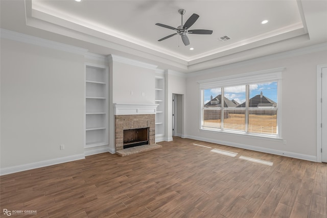 unfurnished living room with ceiling fan, a stone fireplace, crown molding, wood-type flooring, and a tray ceiling