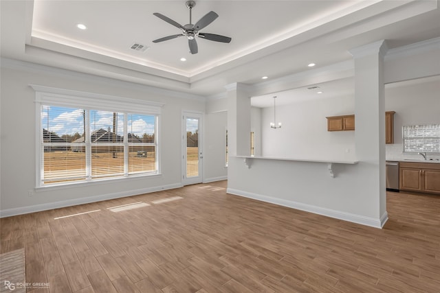 unfurnished living room featuring sink, crown molding, hardwood / wood-style floors, a tray ceiling, and ceiling fan with notable chandelier