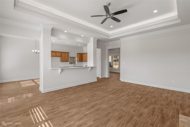 unfurnished living room with ceiling fan with notable chandelier, light hardwood / wood-style flooring, a raised ceiling, and ornamental molding