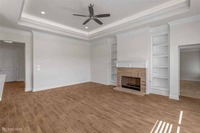 unfurnished living room with light hardwood / wood-style flooring, ceiling fan, ornamental molding, a fireplace, and a tray ceiling