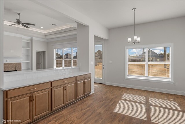 kitchen with pendant lighting, dark wood-type flooring, ceiling fan with notable chandelier, a brick fireplace, and ornamental molding