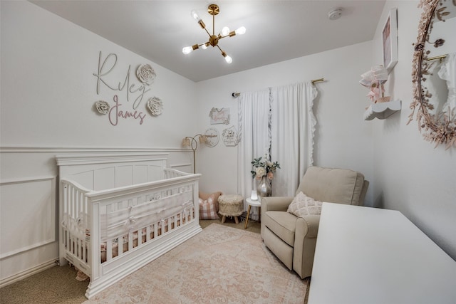 bedroom with light carpet, a nursery area, and an inviting chandelier