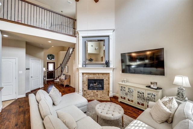 living room featuring wood-type flooring, a towering ceiling, and a tiled fireplace