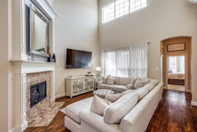 living room with wood-type flooring, a tiled fireplace, and a high ceiling