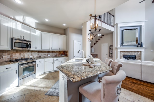 kitchen with a breakfast bar, a center island with sink, white cabinets, sink, and appliances with stainless steel finishes