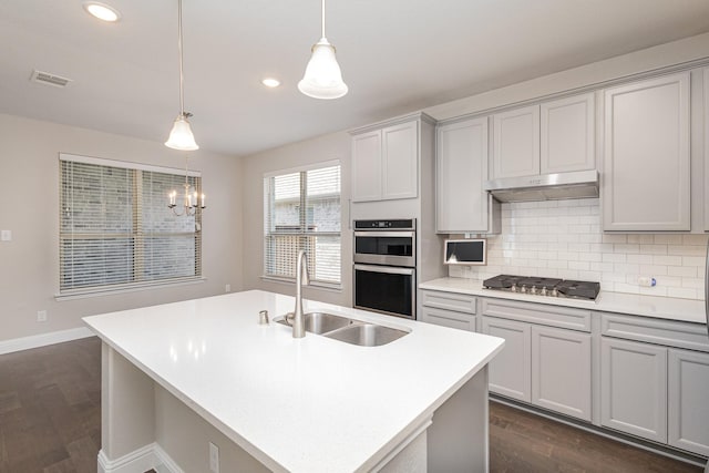 kitchen with stainless steel appliances, decorative light fixtures, a chandelier, dark hardwood / wood-style floors, and an island with sink