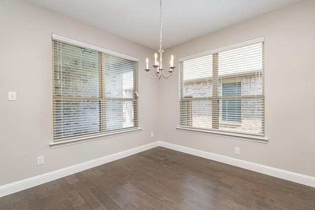 empty room with dark wood-type flooring, a healthy amount of sunlight, and a notable chandelier